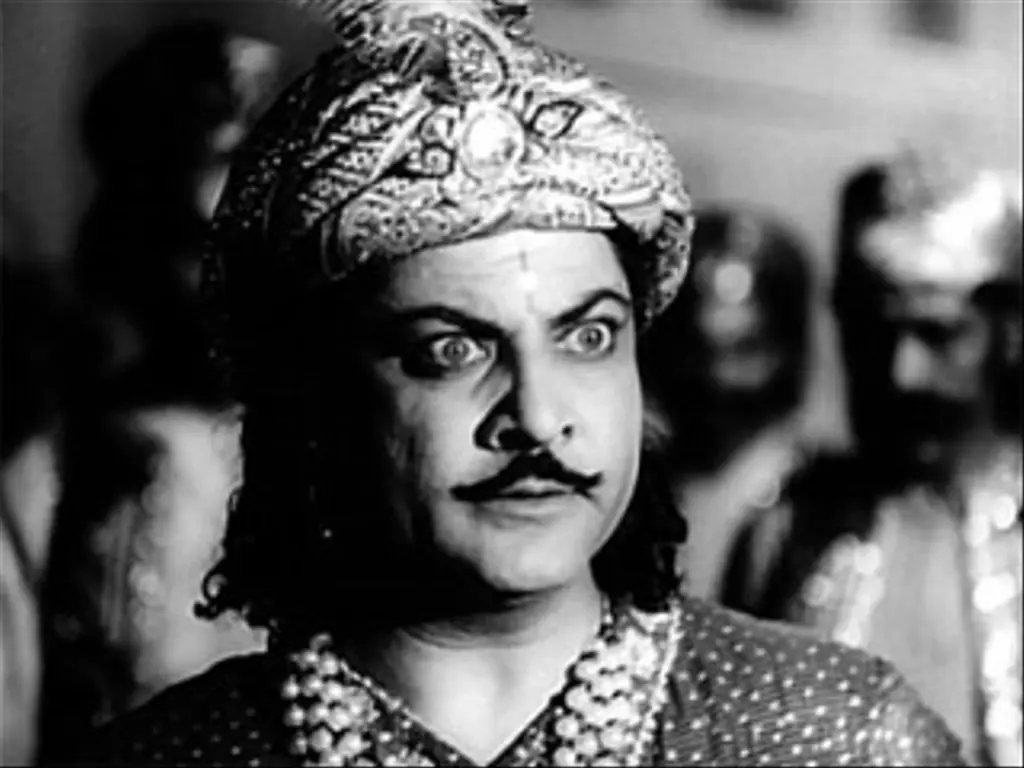 Black and white film still of the actor Chandra Mohan in a jewelled turban, eyes wide, with a moustache.
